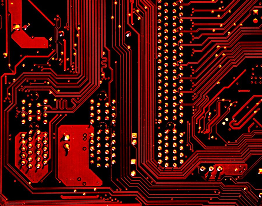 A red and black circuit board with intricate metallic pathways and solder points